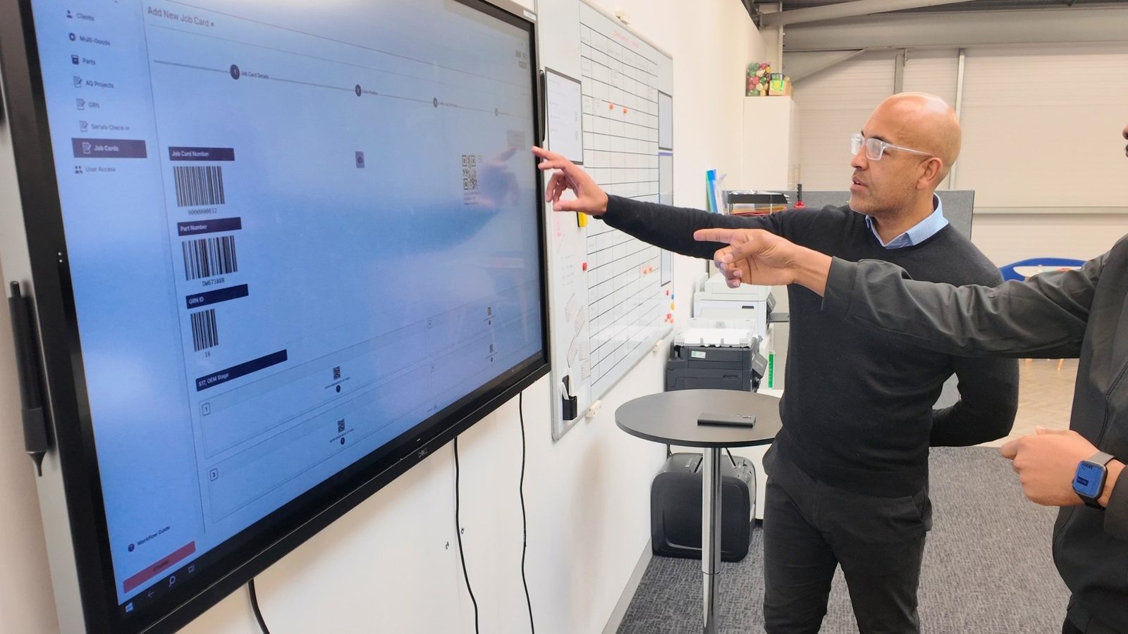 Two colleagues reviewing a job card in MiDAS on a wall-mounted screen