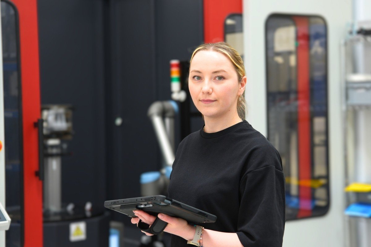 An AddQual engineer holding a rugged tablet in front of an automated inspection cell